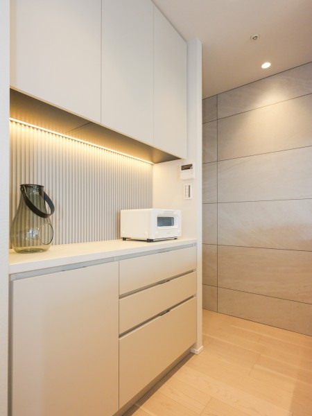キッチンとお揃いのカップボードを設置しているため、作業スペースや収納として活躍してくれそうな空間です。リブパネルを間接照明が照らし、より瀟洒な印象へと演出します。