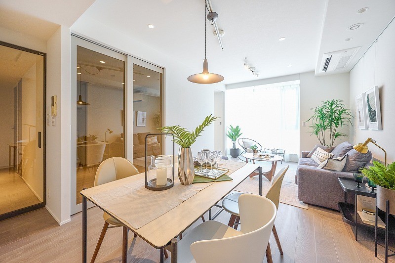 大きな窓から明るく柔らかい陽光が差し込むリビングは、ゆったりとお過ごししやすい仕様となっております。ホワイト調のクロスと木目調のフロアー材が洗練された空間を彩っております。洋室2の扉は、引き戸となっており開放してLDKを拡張してお使いいただけます。