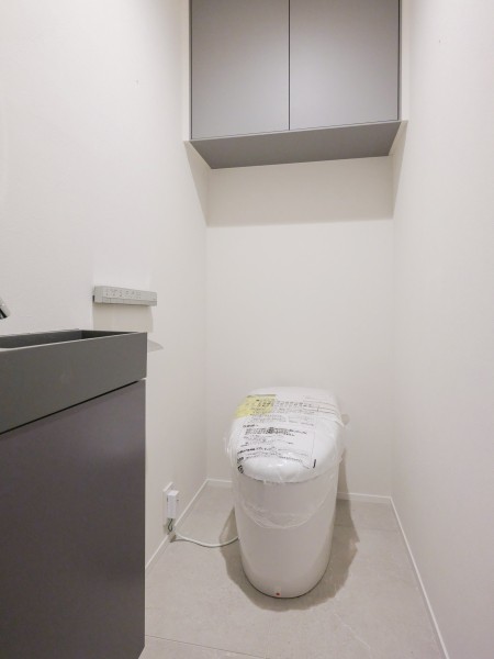 モダンで清潔感溢れるレストルームにはタンクレストイレと吊戸棚、手洗い場を設置いたしました。ダークカラーの吊戸棚と手洗い場がアクセントなっている空間です。