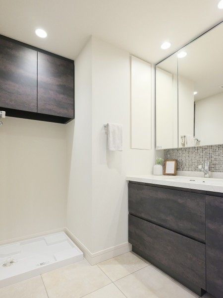 洗面室には洗面化粧台と吊戸棚、リネン庫があり、色数を抑えることでスタイリッシュな空間となっております。洗濯機置き場上の吊戸棚には洗濯グッズを収納することで家事の動線を活かすことができます。