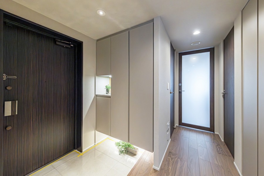 フットライトの光が格調高い雰囲気を醸し出す玄関。カウンターの照明が住まいの顔になってくれます。ゆとりのある廊下には収納を備え付けました。