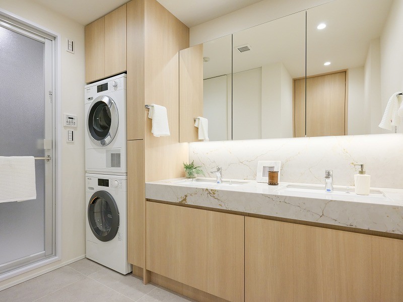 ゆとりある2ボウル設計の洗面化粧台（田中工藝製）と、Miele製のビルトイン洗濯乾燥機。上質な素材と洗練された機能が、朝の支度も快適にサポートします。