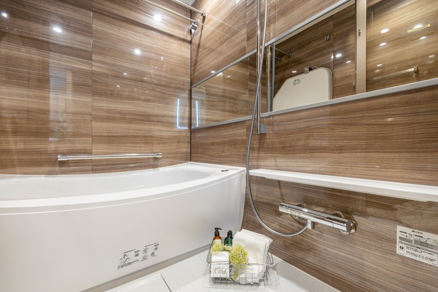 光沢のある木目調パネルが高級感を漂わせるバスルームです。ワイドミラーが空間をより広く感じさせ、一日の疲れをしっかりと癒す安らぎの時間をお楽しみいただけます。