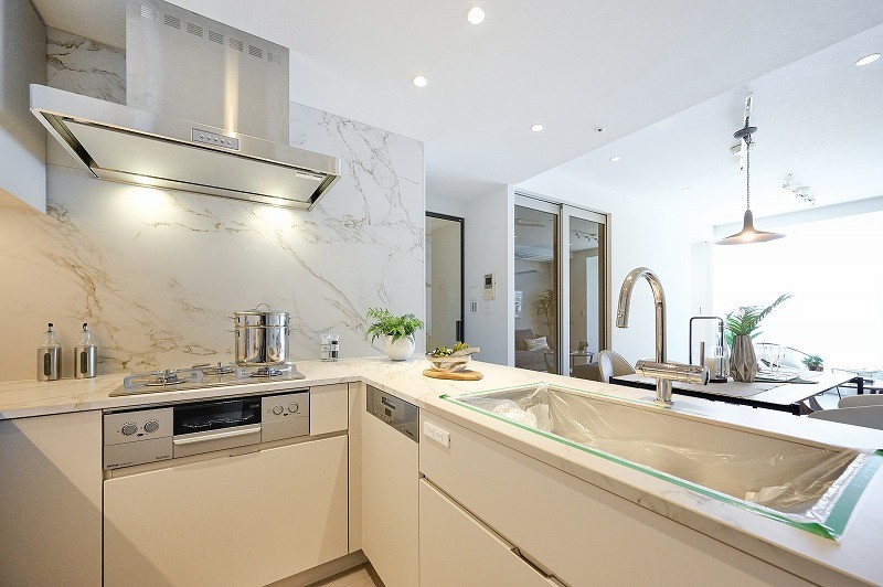 リビングを眺めながらお料理ができるキッチンは田中工藝製のシステムキッチンです。お部屋のホワイトカラーと統一したカラーのシステムキッチンは清潔感を感じさせ、3口コンロとグリル、ディスポーザー付きと嬉しい仕様になっております。