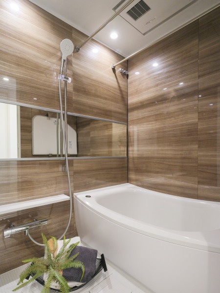 光沢のある木目調パネルが高級感を漂わせるバスルームです。浴槽は美しいカーブと全身を包み込むような入浴感が特長で、快適なバスタイムをお楽しみいただけます。