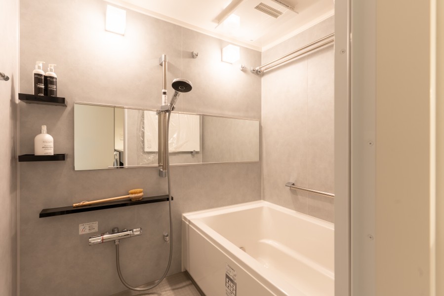 洗練されたグレーの意匠パネルと、ブラックの棚がアクセントを添えるバスルーム。新規交換された清潔感あふれる空間に、モダンな機能美を詰め込みました。