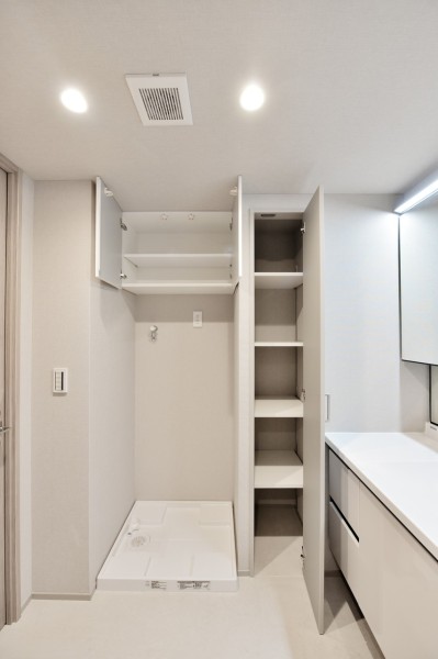 洗面室、洗濯機置場上部にリネン類や洗剤類などを収納できる吊戸棚と棚を設置し、生活感を出さずにあらゆるものが収納できます。ミラー上部のライン照明やダウンライトなどで明るさも十分、メイクもしやすいです。