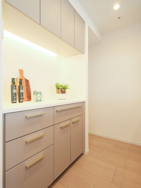 キッチン背面には、デザインを統一した機能的なカップボードを配置しました。食器や調味料がスマートに収まる設計です。棚下灯の光がアクセントとなり、日々使う調理家電やこだわりの雑貨をより魅力的に演出します。