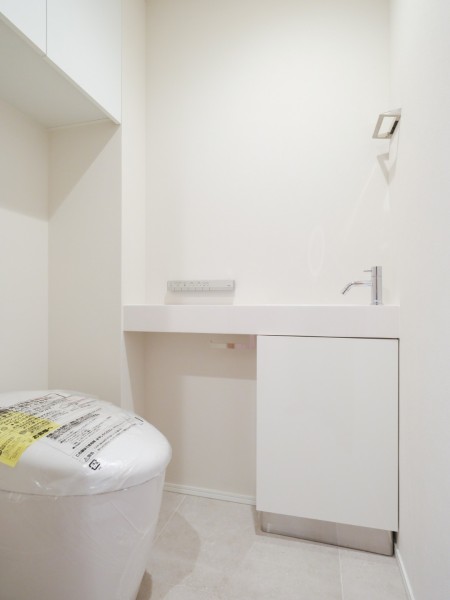 レストルームにはスマートなタンクレストイレを採用しています。上部吊戸棚収納や手洗いカウンターも備え、すっきりとした空間ながらも使いやすさも考慮された設計です。