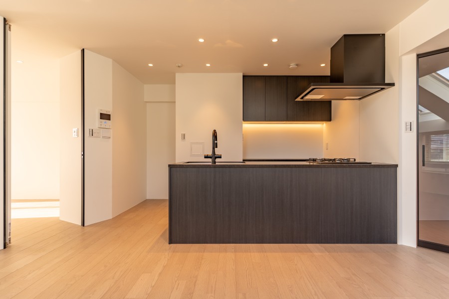 キッチンはダークトーンのアクセントで、洗練された雰囲気を演出します。間接照明が壁面に柔らかな陰影を落とし、空間を広く、優しく見せます。