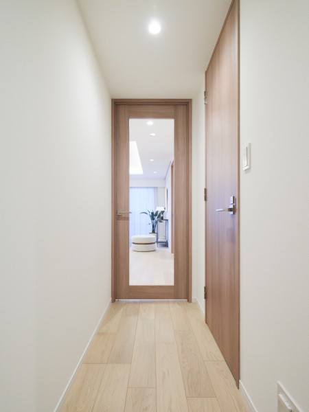 明るい木目の建具とフロアー材が並ぶ廊下です。正面のガラス入り扉が視線を先まで通し、空間に軽やかな印象を与えています。