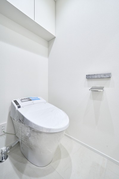 やわらかな色合いでまとめられたレストルームは、清潔感の中に落ち着きを感じられる空間です。トイレットペーパーなどの収納に便利な吊戸棚を備え付けました。