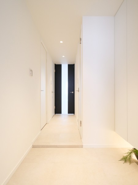 フットライトが足元を優しく照らし、気品漂うホワイト基調で仕上げた玄関スペースです。リビングへとつながるダークトーンの扉が空間のアクセントとなり、先へと続くリビングダイニングへと誘います。