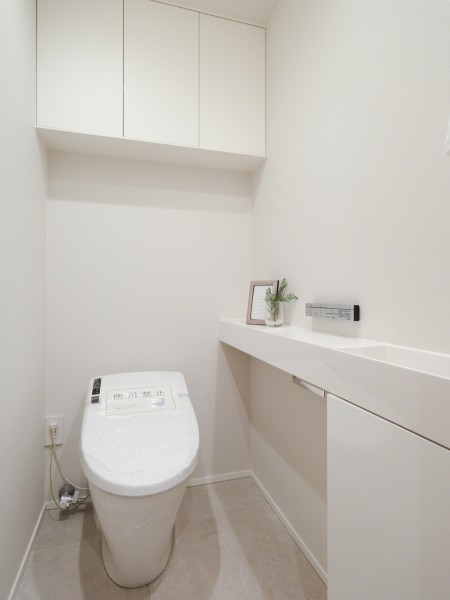 LIXIL製の洗浄便座付きトイレへ新規交換しました。上部には実用的な吊戸棚を設置し、トイレットペーパーやお掃除用品をすっきりと収納できる清潔感のあるシックなレストルームです。